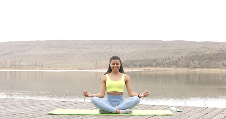 American black sportswoman sitting on lake enjoying fresh air meditating for zen, healthcare. Motivation. Active lifestyle.