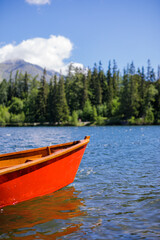 Obraz premium Mountain lake with coniferous forest, wooden boat sunny blue sky, idyllic freedom travel background. Romantic tourist place. National Park High Tatras, Europe. Beautiful nature landscape idyllic view