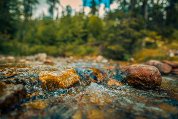 Abstract closeup streaming bubbles over riverbed with colorful stones. Closeup nature background motion, speed, varying textures and vibrant colors. Drops streams of water scatter over the stone.