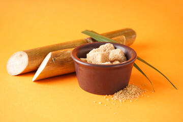 Granulated brown sugar, sugarcane and green leaf on a orange background, closeup.