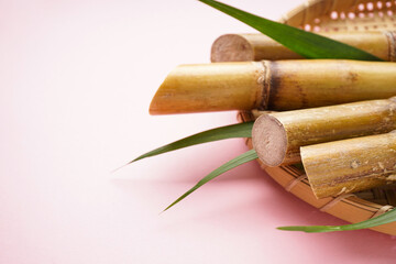 Sugar cane and green leaf in a wooden tray on a pink background, space for text. Closeup