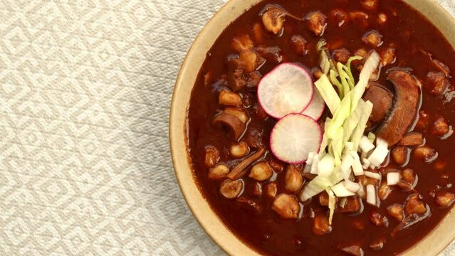 Close-up, top view of vegan Pozole Rojo with lettuce, radish and onion. Famous Mexican cuisine dish made with cacahuazintle, shredded jackfruit, mushrooms and dried chilies: guaillo, ancho, pasilla.