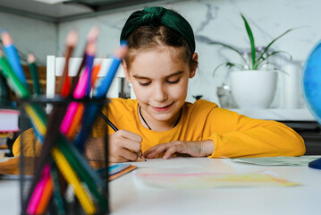 Back to school. Happy cute industrious child girl is sitting at a desk and drawing in home. Kid is learning.