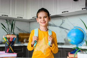 Elementary school student with a blue backpack is standing in the kitchen of the house. The beginning of lessons. The first day of autumn.