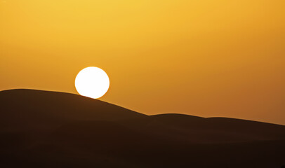 Gold yellow sunset with circular full round sun ball touching silhouette of desert sand dunes sky - Morocco, Erg Chebbi, North Africa