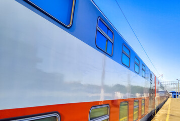 Side of a double-decker train leaving a station in sunny day. 