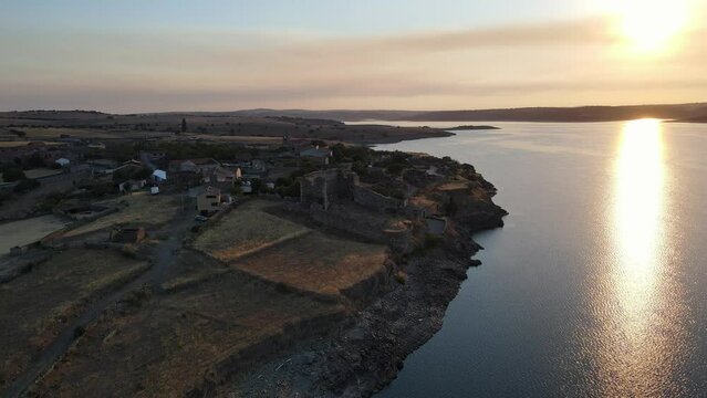 Aerial view of an ancient village on the edge of a lake with calm waters at sunset.