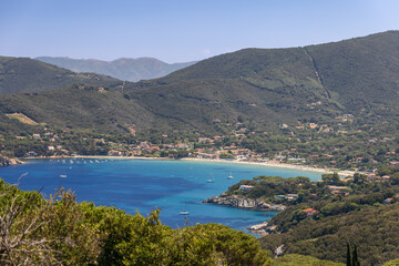 View of gulf and Spiaggia di Procchio, Punta Agnone, village of Procchio and mountains densely overgrown with forest. Province of Livorno,  Island of Elba, Italy
