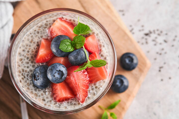 Chia strawberry pudding. Healthy vegan breakfast chia seeds pudding with fresh berries and mint in glass on gray concrete background. Concept of healthy eating, dieting, fitness menu. Selective focus.