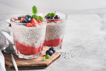 Chia strawberry pudding. Healthy vegan breakfast chia seeds pudding with fresh berries and mint in glass on gray concrete background. Concept of healthy eating, dieting, fitness menu. Selective focus.