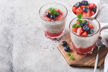 Chia strawberry pudding. Healthy vegan breakfast chia seeds pudding with fresh berries and mint in glass on gray concrete background. Concept of healthy eating, dieting, fitness menu. Selective focus.