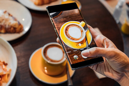 Hand of woman taking a photo of cup coffee with a mobile phone