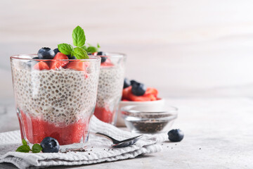 Chia strawberry pudding. Healthy vegan breakfast chia seeds pudding with fresh berries and mint in glass on gray concrete background. Concept of healthy eating, dieting, fitness menu. Selective focus.
