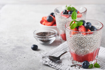 Chia strawberry pudding. Healthy vegan breakfast chia seeds pudding with fresh berries and mint in glass on gray concrete background. Concept of healthy eating, dieting, fitness menu. Selective focus.