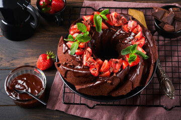 Dark Chocolate Bundt Cake with Ganache Icing and strawberry on dark stone or concrete table background. Festive cake. Selective focus