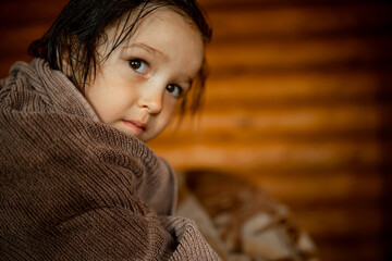 Cute baby sits on bed, wrapped in a towel after bathing