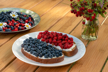Sandwiches with wild berries collected in the forest. Blueberries and strawberries on cream cheese for breakfast. Summer concept.