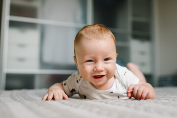 Portrait of a crawling baby on the bed in room. Adorable baby boy in bedroom. Newborn child relaxing. Nursery for children. Family morning at home.