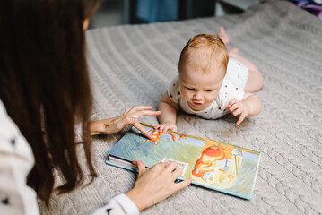 Portrait of mother and baby boy read book in bed at home. Mom with son.