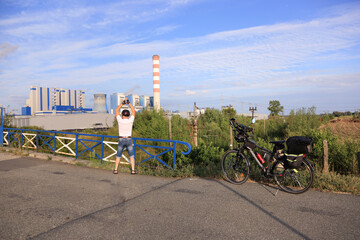 Mężczyzna z podniesionymi rękoma i rowerem turystycznym na wiadukcie, elektrownia.