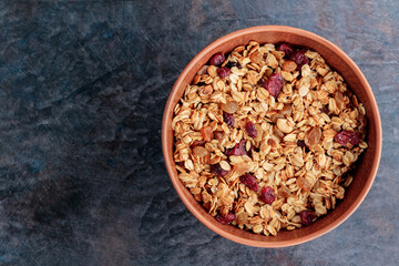 Granola with nuts and dried fruit on a dark background. Homemade granola in a clay bowl. Top view....