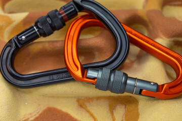 Orange and black aluminum carabiners on a climbing fingerboard