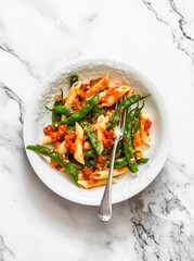 Vegetarian penne pasta with green beans and tomato sauce on a light background, top view
