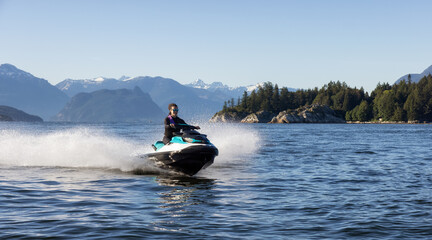 Adventurous Caucasian Woman on Water Scooter riding in the Ocean. Howe Sound and mountain landscape in background. West Vancouver, British Columbia, Canada.