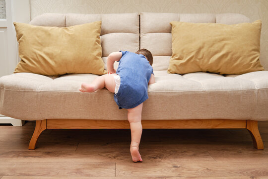 Toddler Baby Climbs On The Sofa. Child Boy Learning To Get Off The Bed. Kid Age One Year