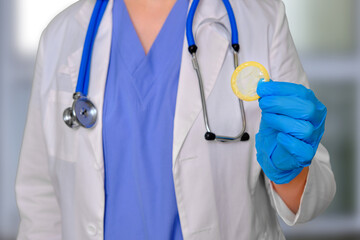 Woman doctor holding a condom in her hand as a contraceptive, clinic background