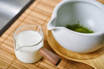 Matcha tea powder in white clay tea bowl with milk, Matcha latte ingredients, Green tea making set, Japanese ceremony traditional drink.