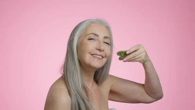 Beauty care procedures. Happy beautiful grey haired senior lady doing skin lifting massage with gouache stone