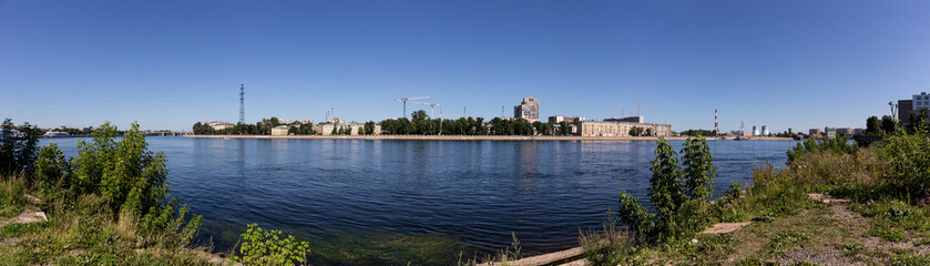 Fototapeta na wymiar Panoramic view of the embankment of the Neva River in St. Petersburg in the Nevsky district near the river station with a view of the pipes of the thermal power plant and building cranes.