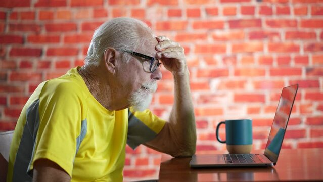 Side view profile of unhappy elderly old man sitting at desk using laptop computer tired and getting bad news.