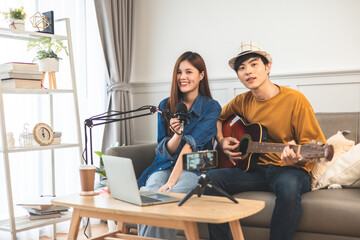 Young couple in headset sing song play guitar streaming at real time on personal music channel at social media.Attractive couple sitting on sofa with a guitar.