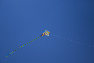 Image of a colorful kite flying high in the sky with a drawing of a smiling sun and a rainbow

