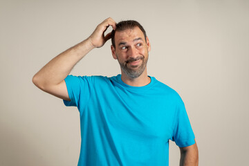 Doubtful bearded latin man thinking, scratching his head and trying to find a solution, isolated on beige background.