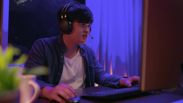 esport online game streaming asian male wear headset play dogital metaverse cyber space online match compettition sport game battle night time,young asia male enjoy exited gamer successful celebration