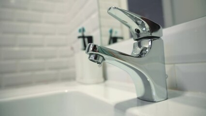 Water leak concept. Static video of a silver faucet in a bathroom with dripping water. Faucet malfunction, drops of clean water dripping into the white washbasin