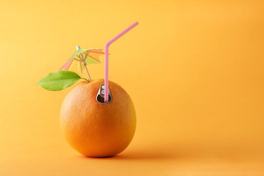 Summer creative concept with copy space. Juicy orange with straw and umbrella on orange background.
