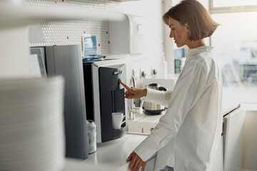 Fototapeta premium Business woman in casual clothes making a coffee in office kitchen during break. High quality photo