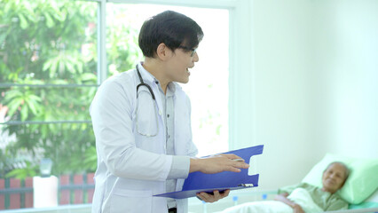 Asian doctor reading a medical document on notepad in hospital treatment ward.