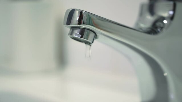 Water leak concept. Close up of water drops.Video of a faucet in a bathroom with dripping water. Faucet malfunction, drops of clean water dripping into the white washbasin