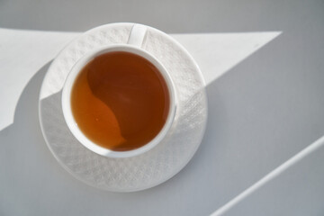 breakfast concept. white embossed cup of tea coffee on white background, sunlight morning, hard shadows. side view, horizontal photo, copy space, minimalism