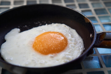 two 2 Fried salt eggs in skillet pan on blue checkered background close up, top view, breakfast food concept.