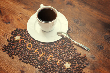 A cup of aromatic coffee and coffee beans on a wooden table.