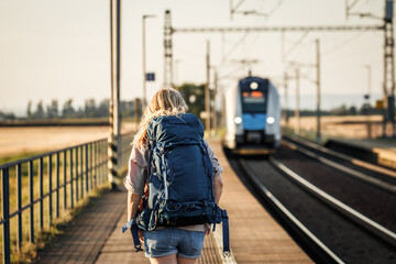 Tourist with backpack looking at arriving train at railroad station