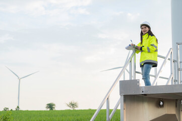 women engineer working and holding the report at wind turbine farm Power Generator Station on mountain,Thailand people