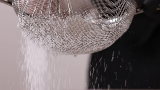 Chef confectioner sifting with whisk white flour or sugar powdered with steel sieve for pie, french dessert macarons or macaroons and cupcake making. slow motion. cooking desserts with sugar powder.