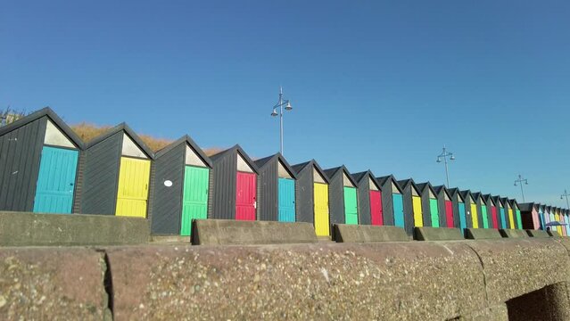 Reveal shot of colourful beach huts on Lowestoft promenade on a bright and sunny morning